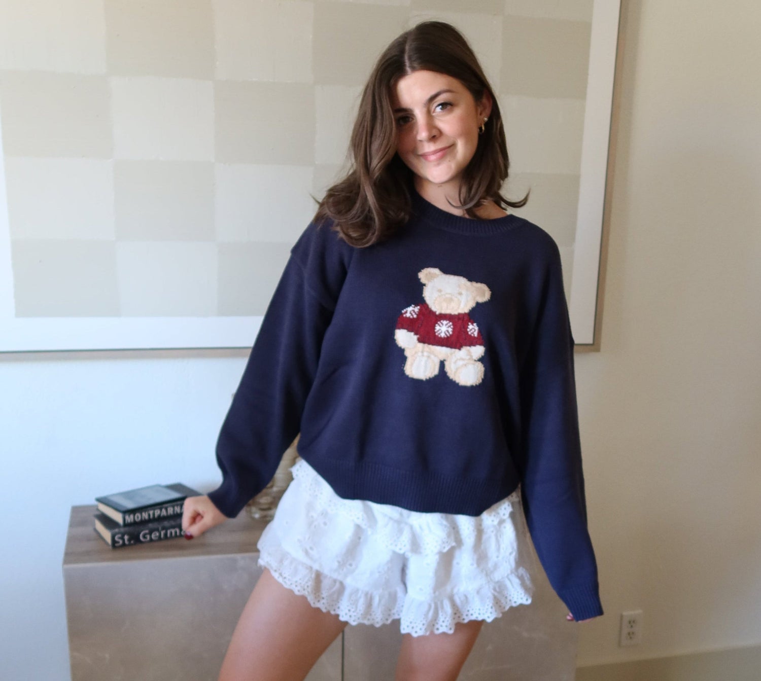 Woman wearing a navy sweater with teddy bear design and a white skirt in a room.